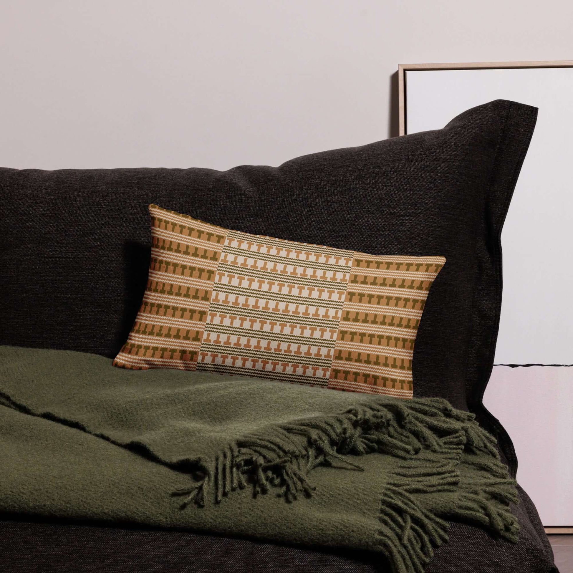 The Amari lumbar throw pillow is shown against a dark couch with a mossy green throw blanket to show how to style the pillow.