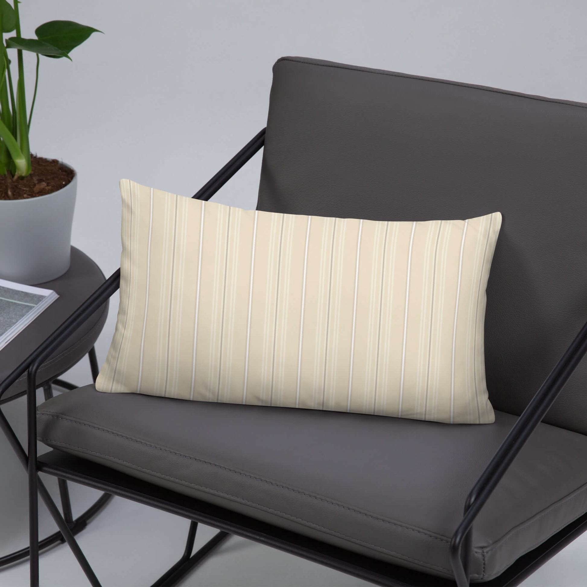 The Joseph decorative lumbar throw pillow is pictured in a modern accent chair with a side table and plant. The pillow has a striped pattern on the front and a plaid design on the back.
