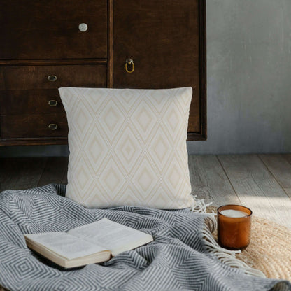 The Reid diamond LOOM Collection pillow is shown on top of a blanket along with a book and a candle.