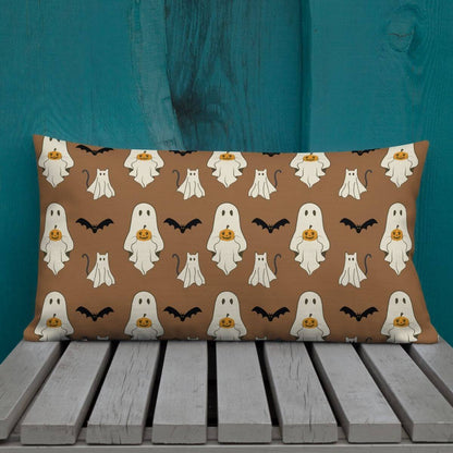 Halloween-themed pillow with ghosts, cats, and bats on a brown background, placed on a wooden surface against a teal wall.