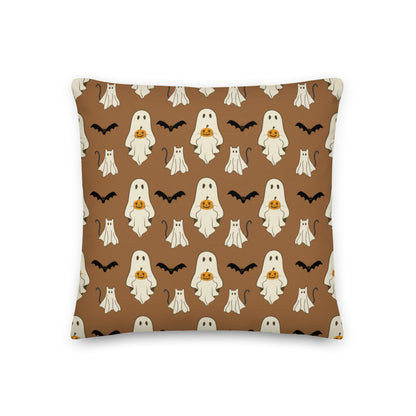Halloween pillow with ghosts, cats, bats, and pumpkins against a brown background.