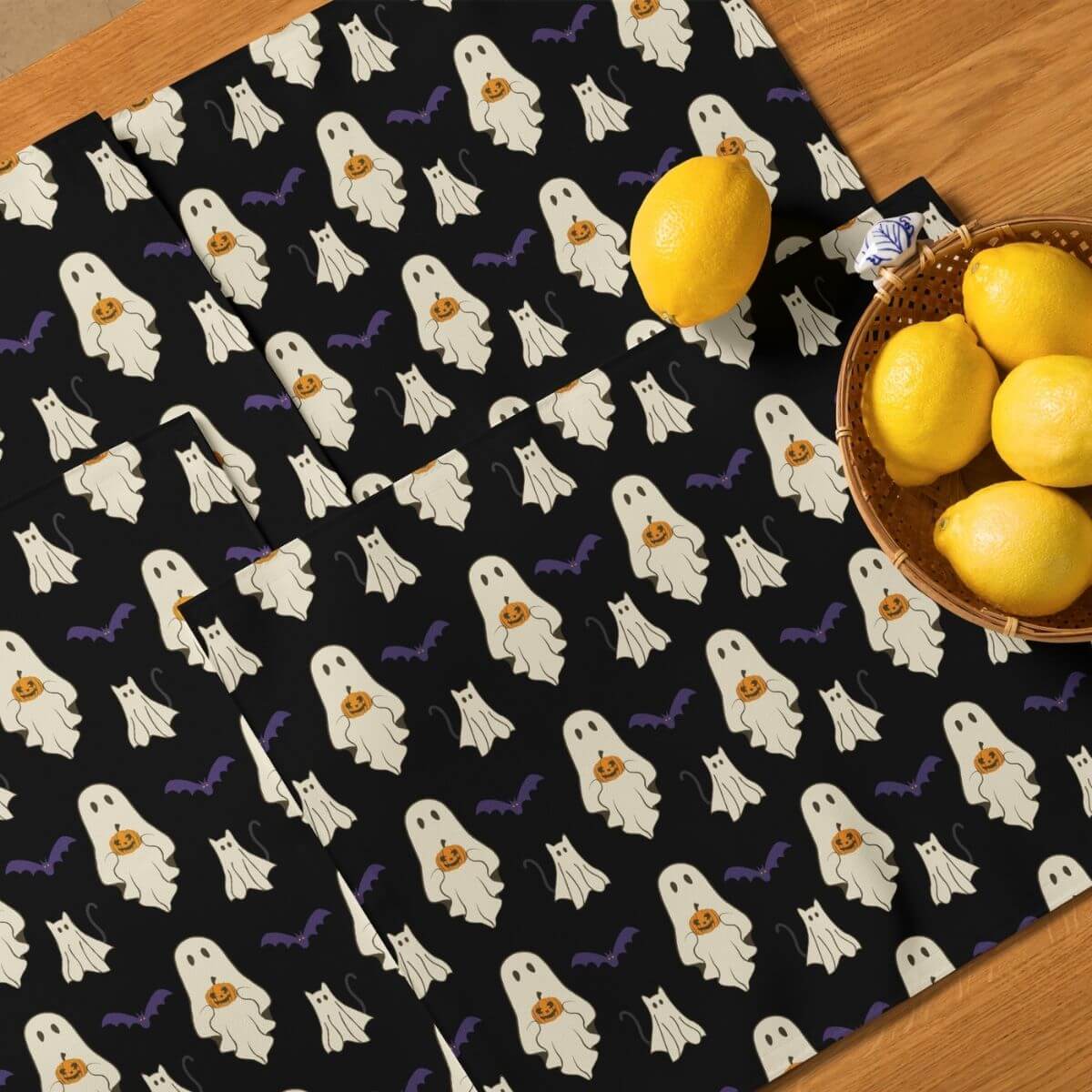Halloween-themed placemats with ghosts and bats on a black background, featuring lemons and a basket of lemons on a wooden surface.