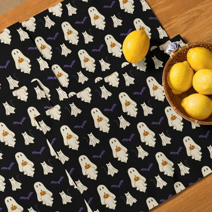 Halloween-themed placemats with ghosts and bats on a black background, featuring lemons and a basket of lemons on a wooden surface.