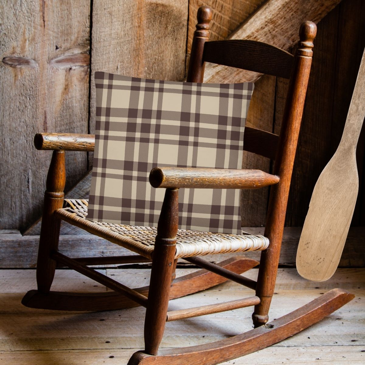 The playful and cozy Atticus pillow is shown in a wooden rocking chair in a lake house, with the pillow flipped to show the classic plaid pattern on the back side.