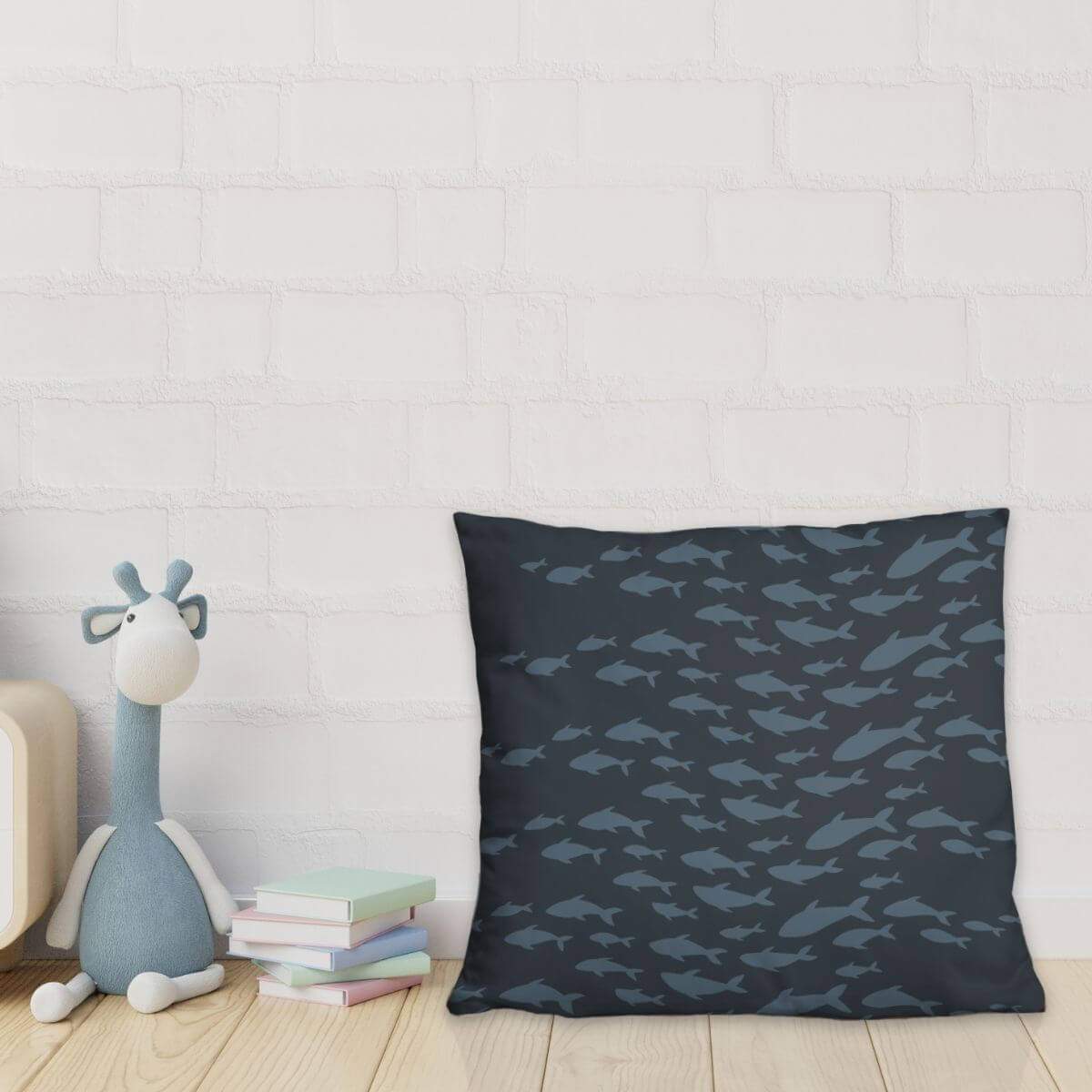 Navy blue pillow with fish pattern next to a plush toy and books on a light wooden floor.