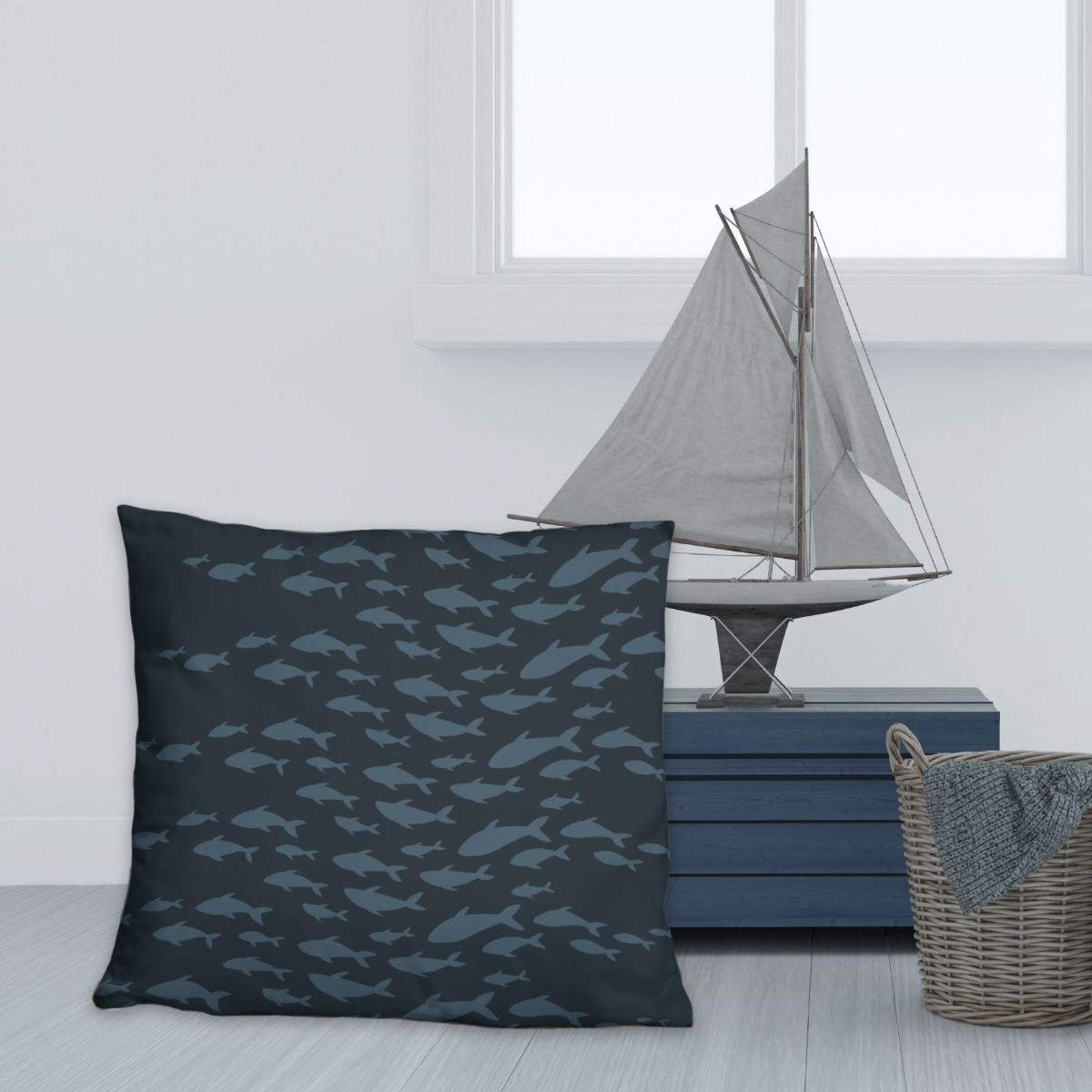 Navy blue throw pillow with fish pattern in an ocean blue shown with a model sale boat and woven basket.