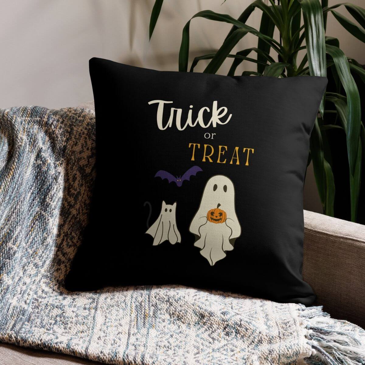 Black pillow with Halloween design featuring ghosts and text on a couch.