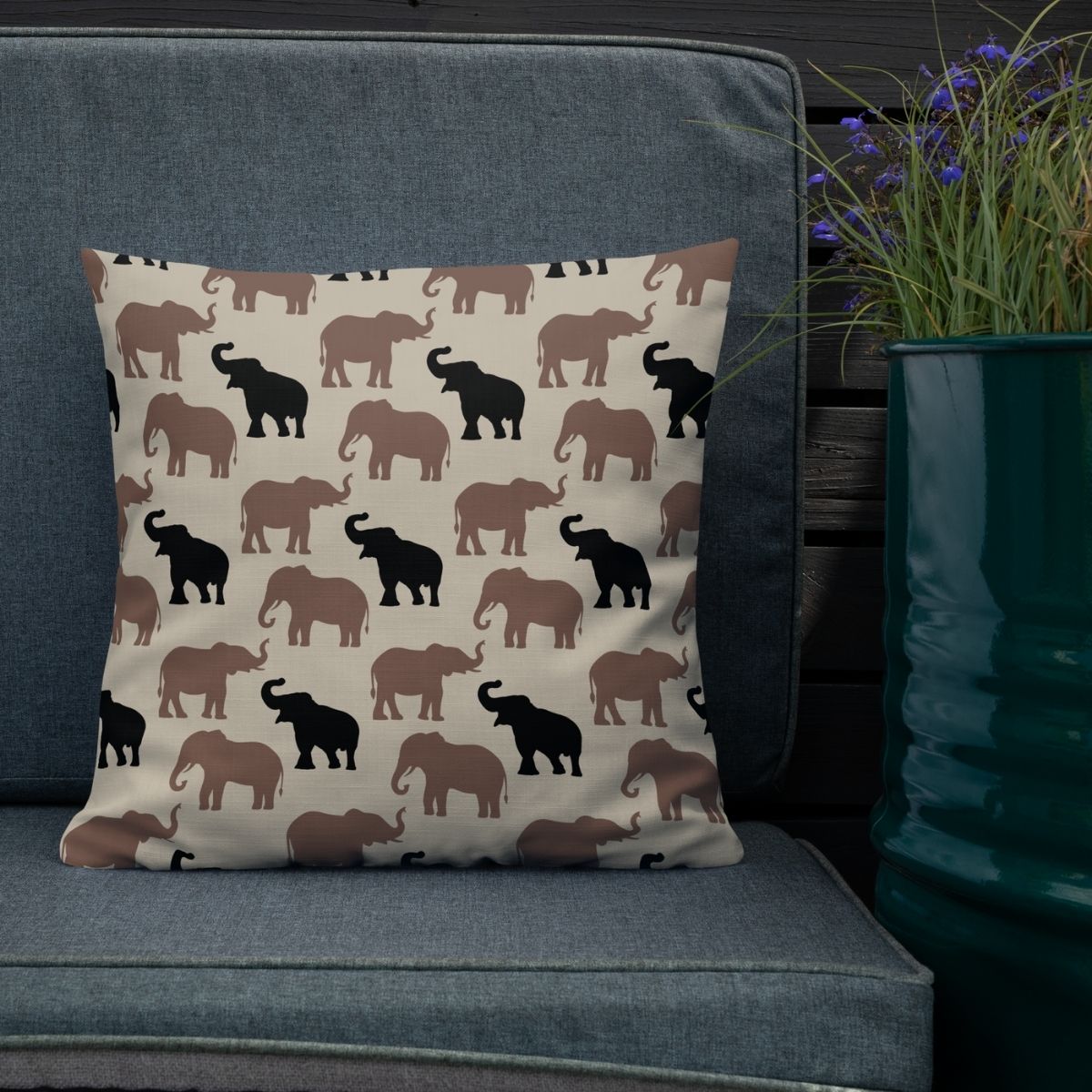 Double-sided throw pillow with elephant pattern on the front and striped on the back resting on a gray chair next to a plant