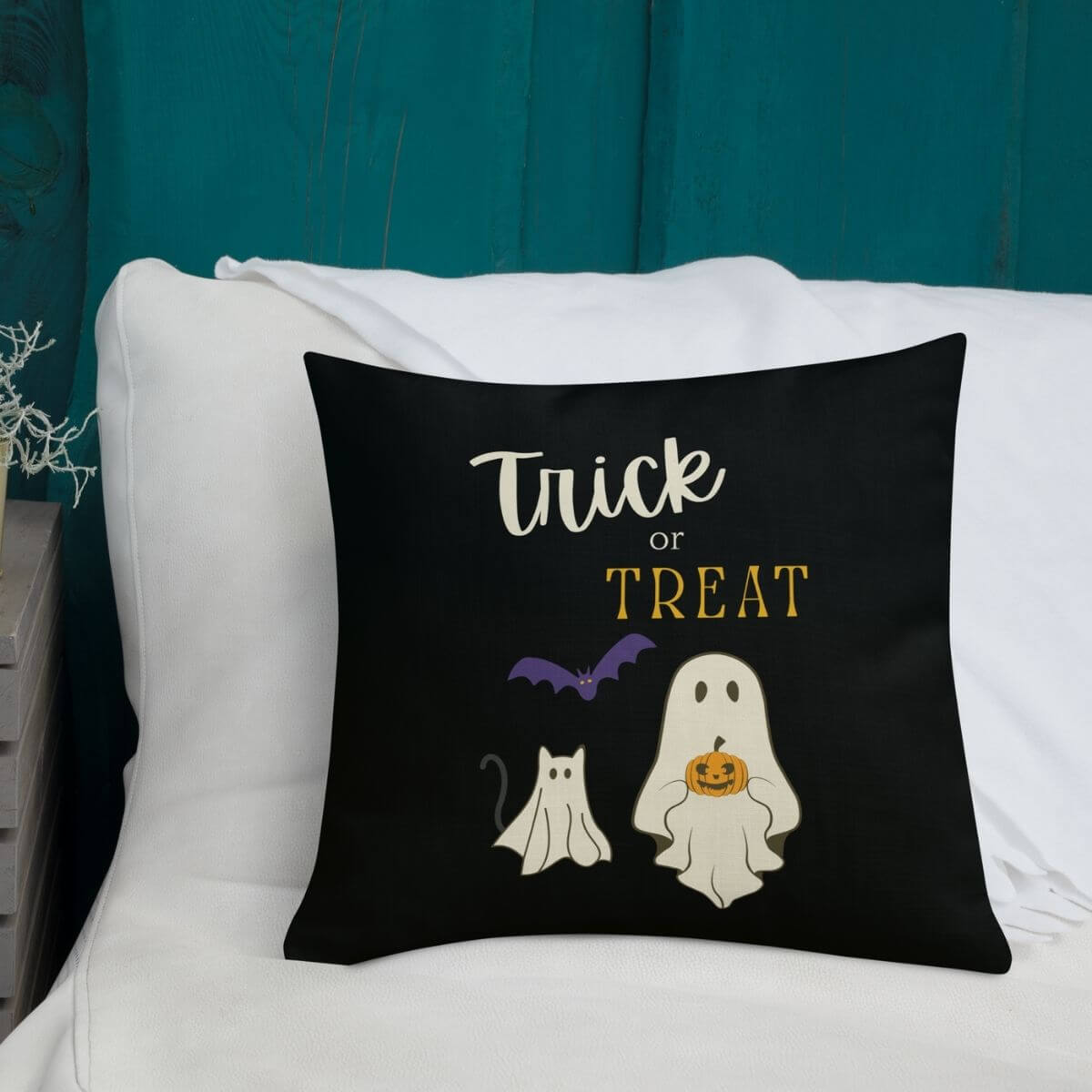 Halloween-themed pillow with 'Trick or Treat' text and ghost illustrations on a white couch.