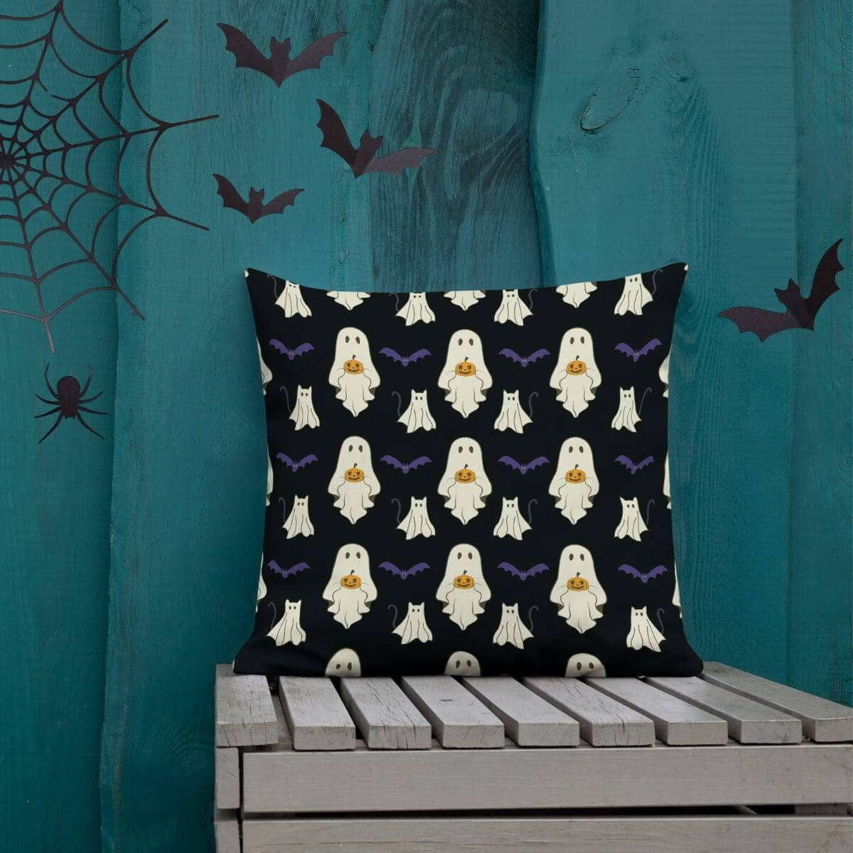 Halloween-themed pillow with ghost pattern on a wooden bench against a teal curtain background.
